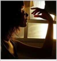Woman in profile with her hand raised beside a sunlit window