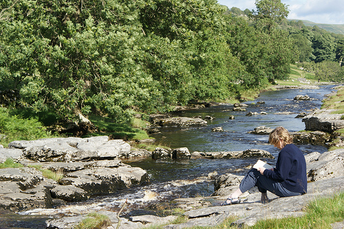 Woman reading beside a stream
