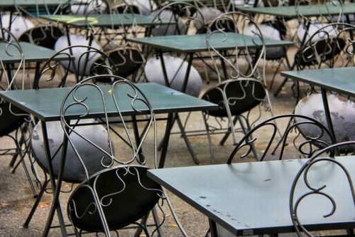 Empty cafe tables with the chairs leaned against them.