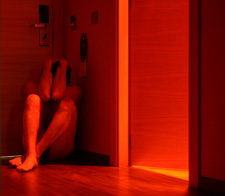 man crouching in a corner covering his face in a room with a red light