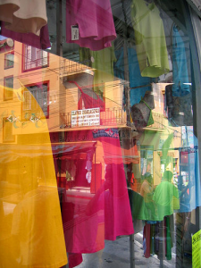 Reflections in a store window with colourful dresses.
